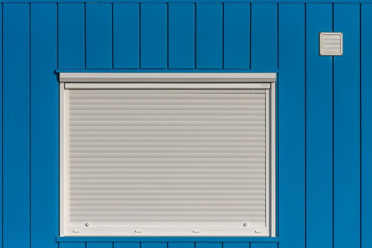 White roller shutter closed over a window on a blue wall