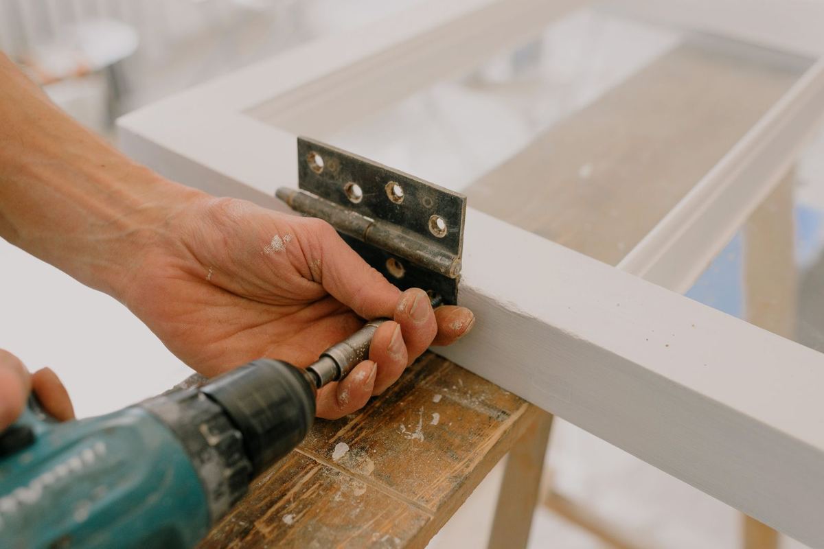 Fitter drilling a hinge on a white window frame